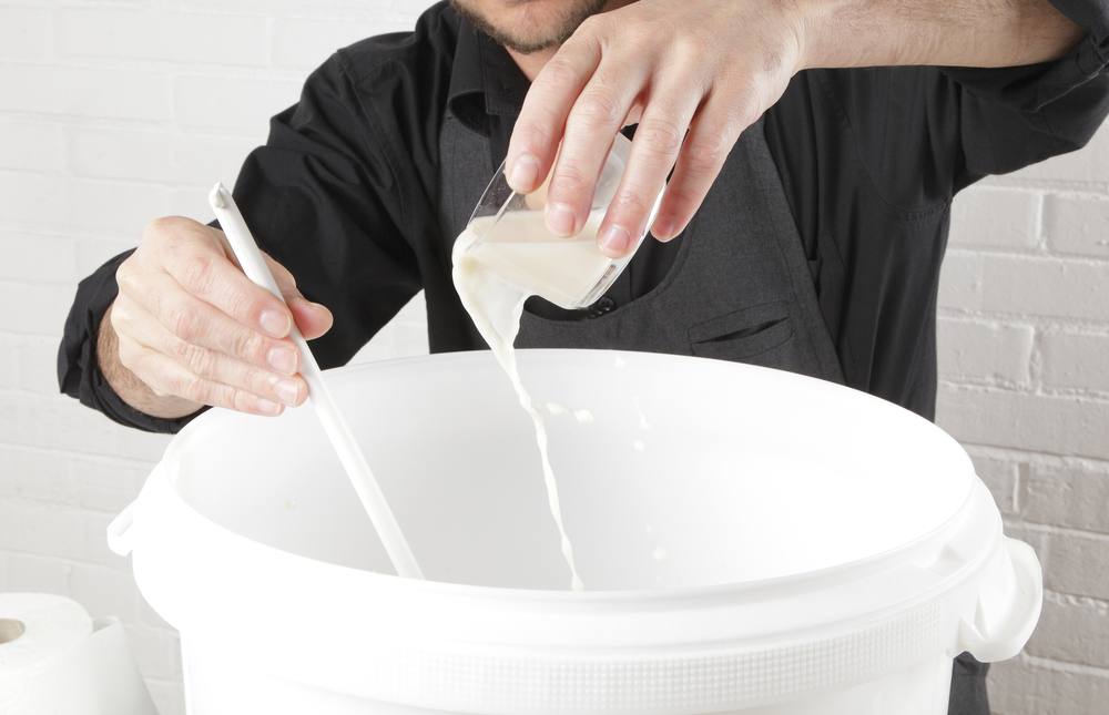 man pouring yeast solution into white plastic brew bucket for fermenting beer